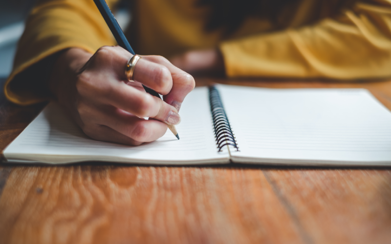 Woman writing in spiral notebook.